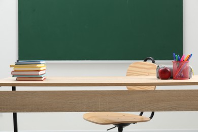Photo of Different school stationery and red apple on wooden table near blackboard indoors