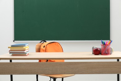 Photo of Different school stationery and red apple on wooden table near blackboard indoors