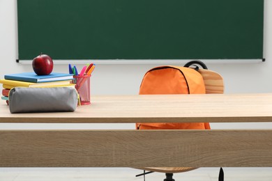 Photo of Different school stationery and red apple on wooden table near blackboard indoors