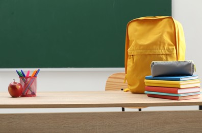 Photo of Different school stationery, backpack and red apple on wooden table near blackboard indoors