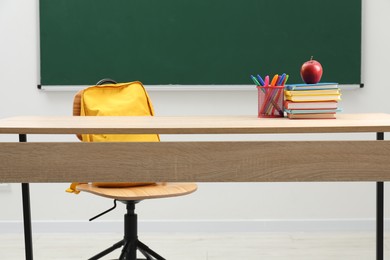 Photo of Different school stationery and red apple on wooden table near blackboard indoors