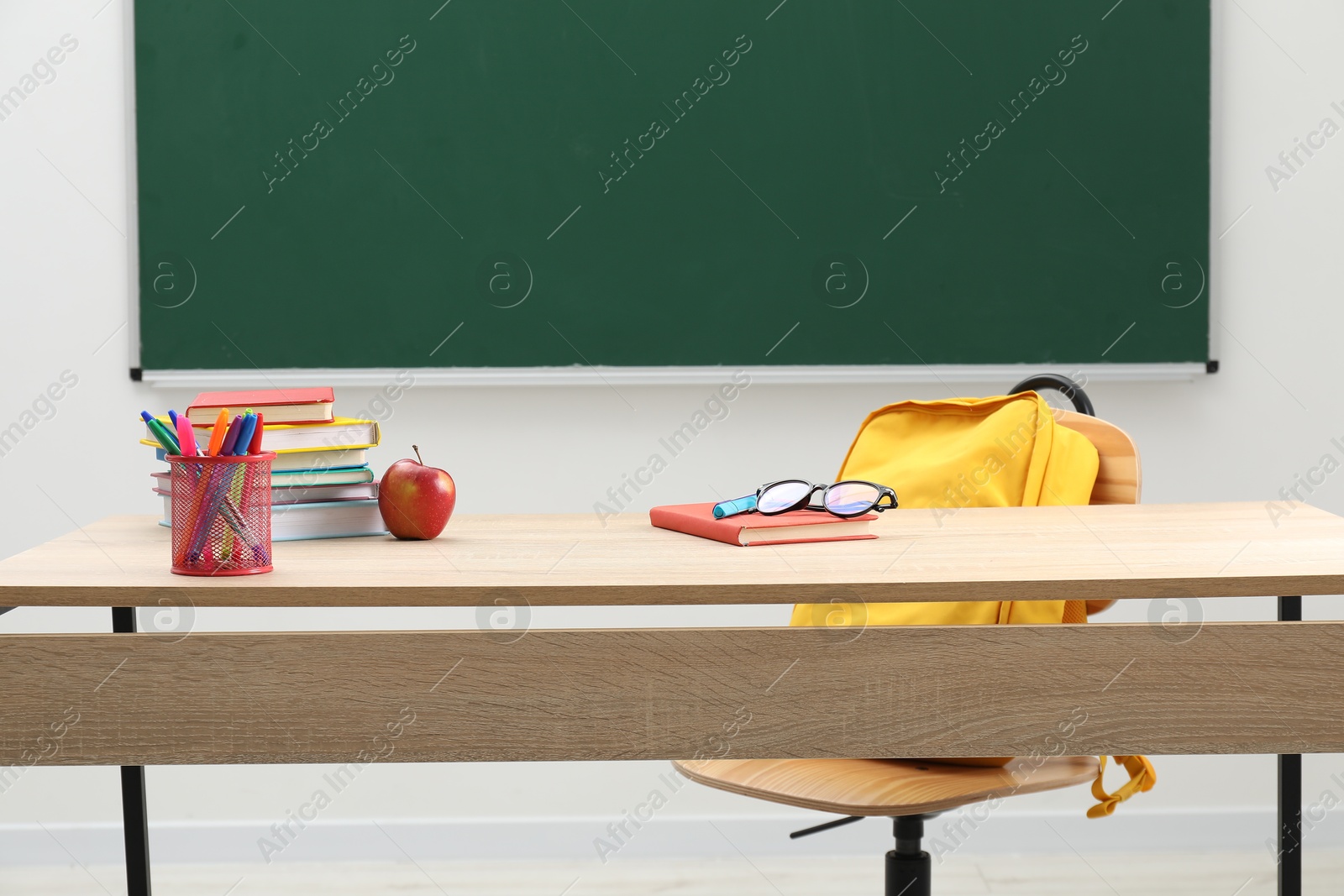 Different school stationery, glasses and red apple on wooden table near blackboard indoors Photo of Different school stationery, glasses and red apple on wooden table near blackboard indoors