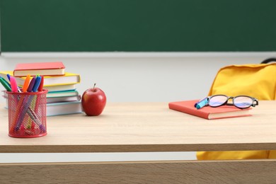 Photo of Different school stationery, glasses and red apple on wooden table near blackboard indoors