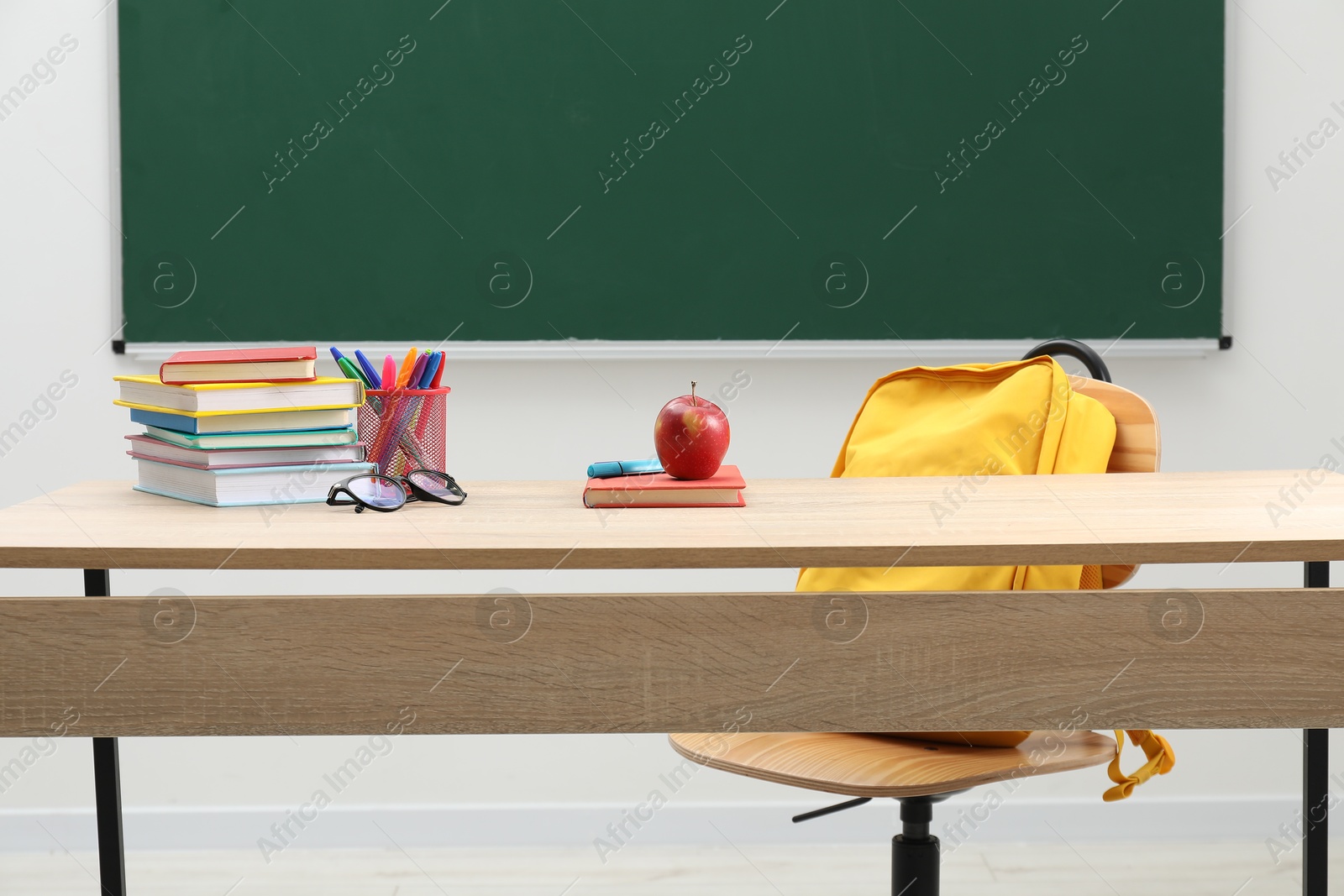 Different school stationery, glasses and red apple on wooden table near blackboard indoors Photo of Different school stationery, glasses and red apple on wooden table near blackboard indoors