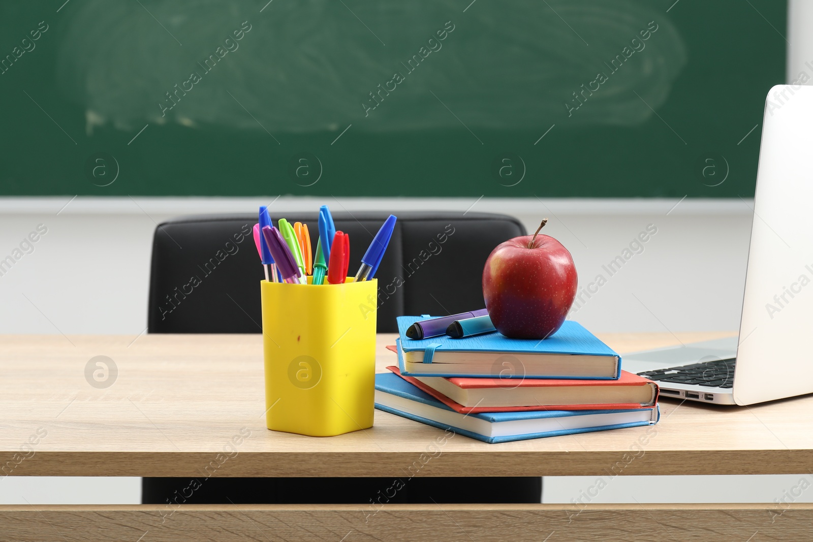 Different school stationery, laptop and red apple on wooden table near blackboard indoors Photo of Different school stationery, laptop and red apple on wooden table near blackboard indoors