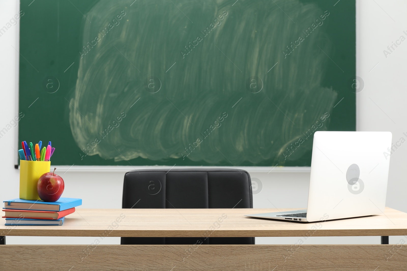 Different school stationery, laptop and red apple on wooden table near blackboard indoors Photo of Different school stationery, laptop and red apple on wooden table near blackboard indoors