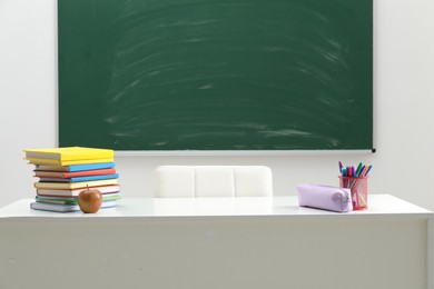 Photo of Different school stationery and apple on white table near blackboard indoors
