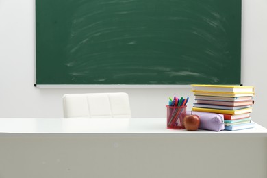 Photo of Different school stationery and apple on white table near blackboard indoors