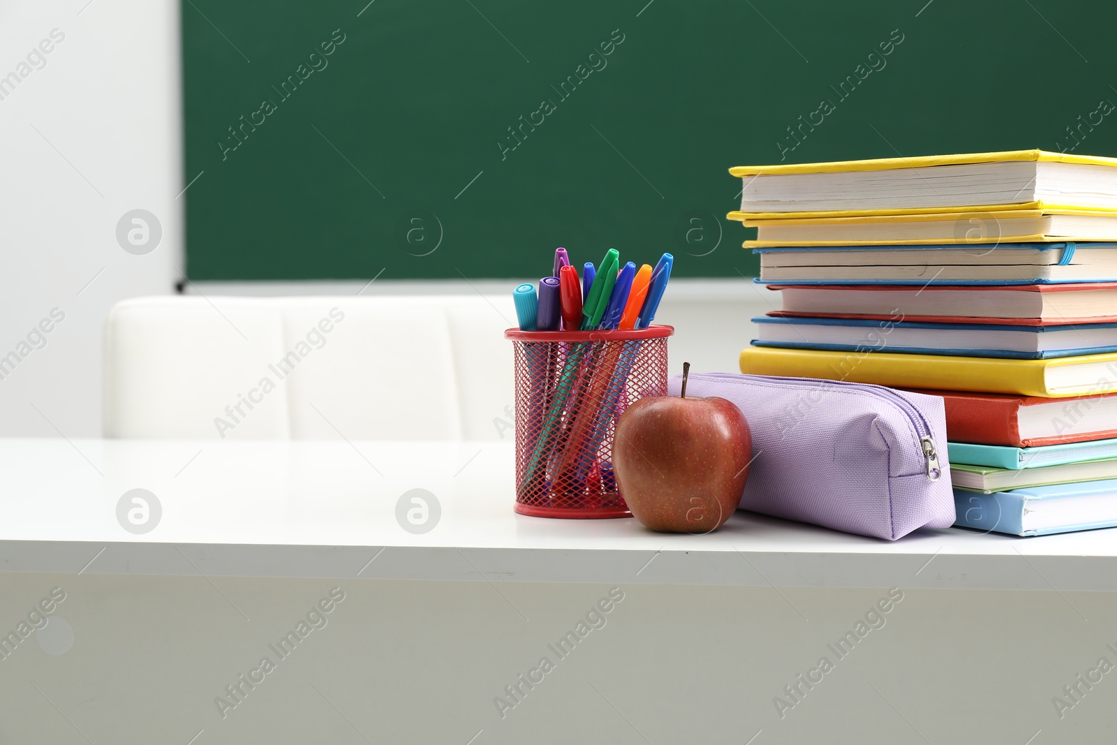 Different school stationery and apple on white table near blackboard indoors, space for text Photo of Different school stationery and apple on white table near blackboard indoors, space for text