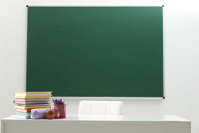 Photo of Different school stationery and apple on white table near blackboard indoors
