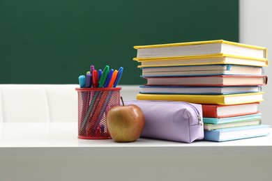Photo of Different school stationery and apple on white table near blackboard indoors