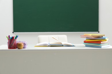 Photo of Different school stationery and apple on white table near blackboard indoors