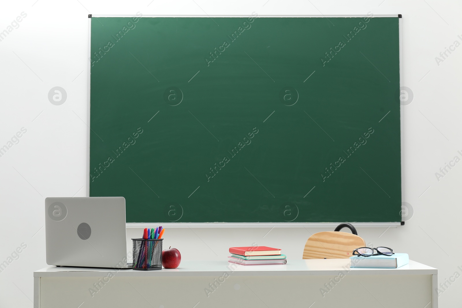 Different school stationery, laptop, glasses and red apple on white table near blackboard indoors Photo of Different school stationery, laptop, glasses and red apple on white table near blackboard indoors