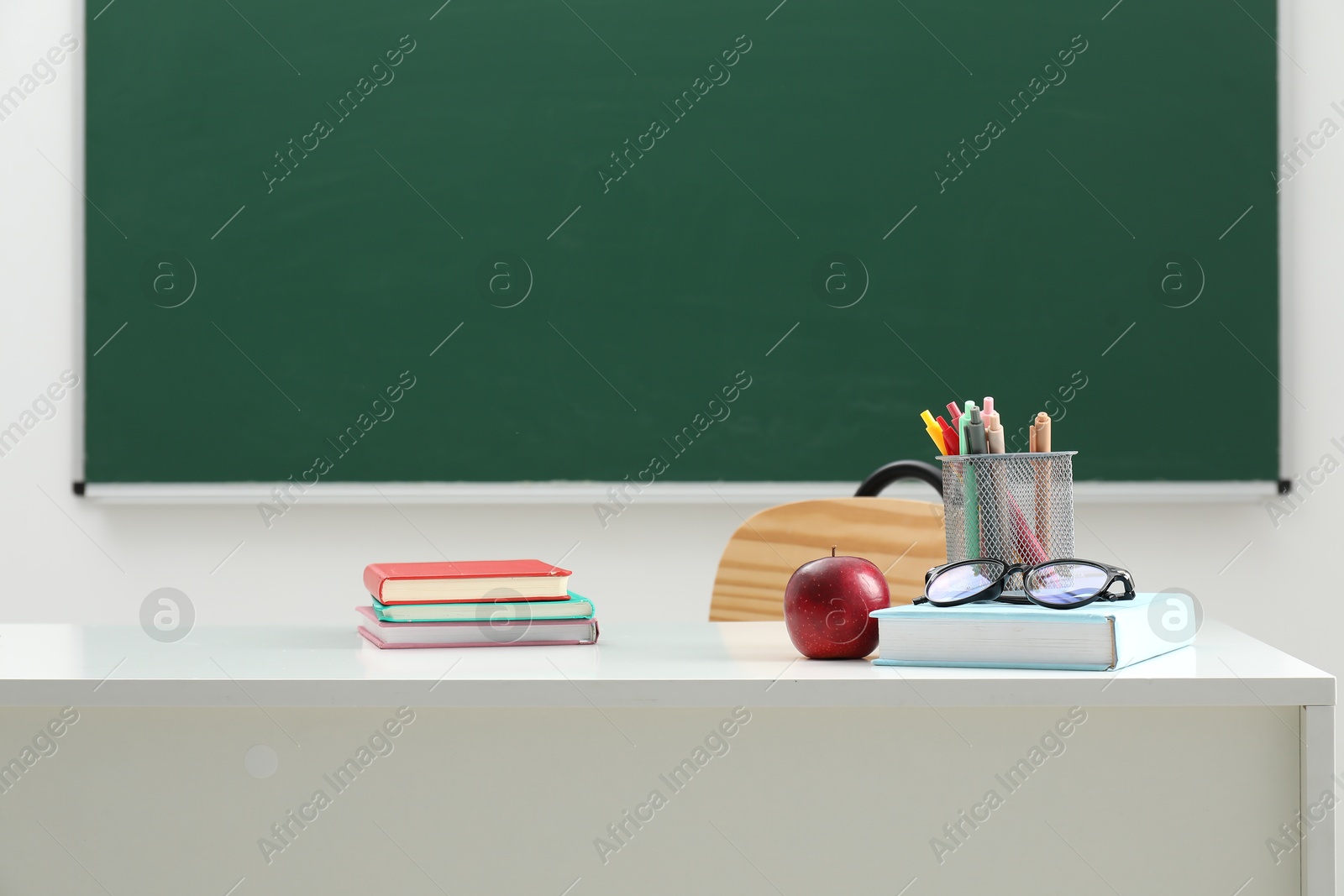 Different school stationery, glasses and red apple on white table near blackboard indoors Photo of Different school stationery, glasses and red apple on white table near blackboard indoors