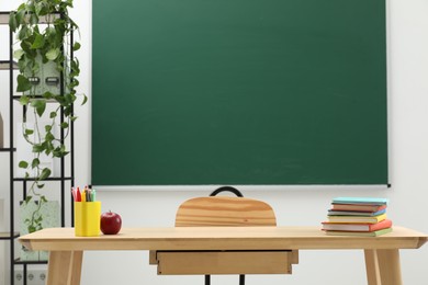 Photo of Different school stationery and red apple on wooden table near blackboard indoors