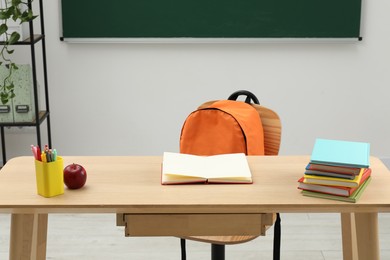 Photo of Different school stationery and red apple on wooden table near blackboard indoors