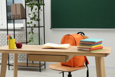 Photo of Different school stationery and red apple on wooden table near blackboard indoors