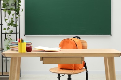 Photo of Different school stationery and red apple on wooden table near blackboard indoors