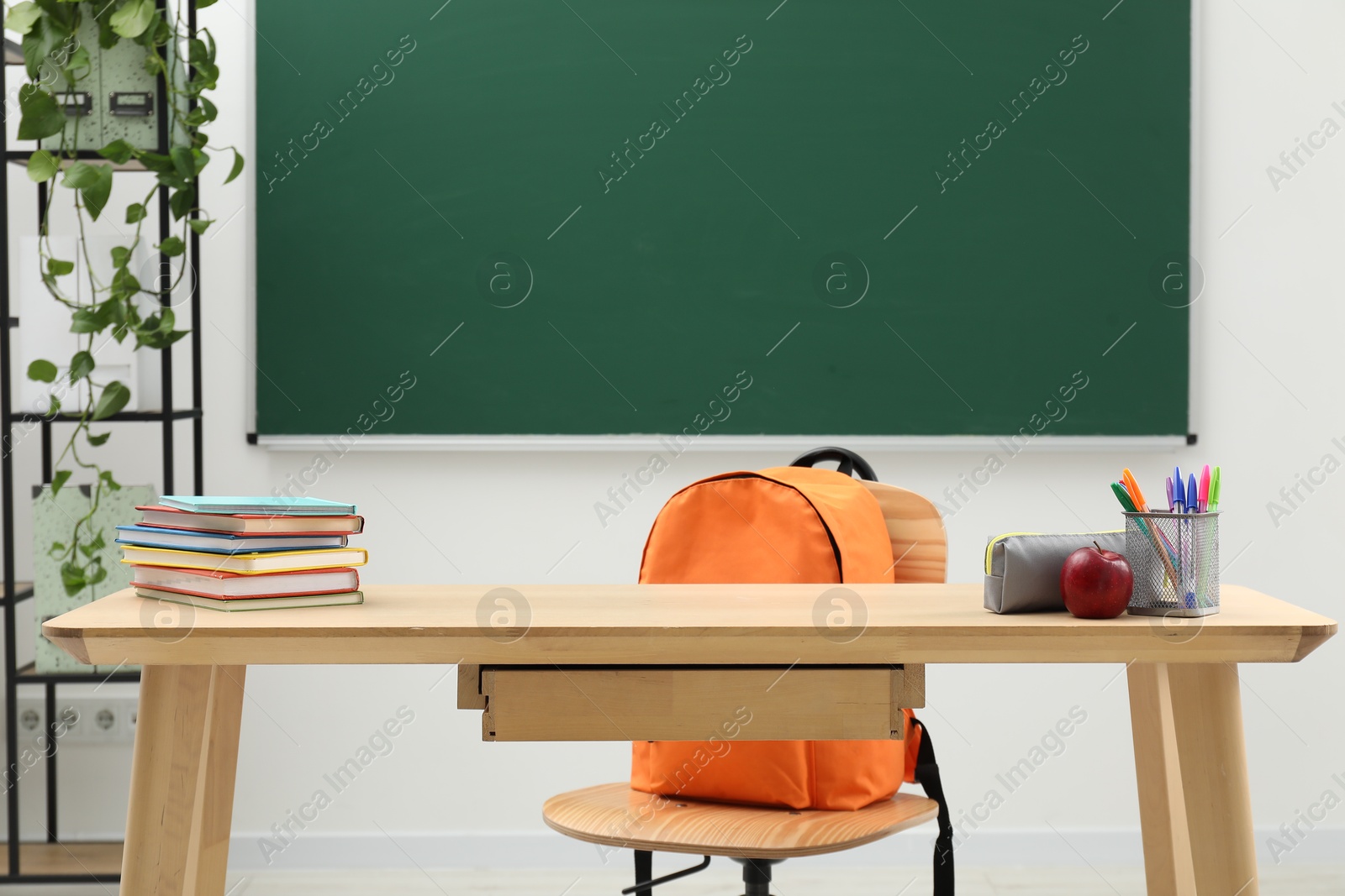 Different school stationery and red apple on wooden table near blackboard indoors Photo of Different school stationery and red apple on wooden table near blackboard indoors