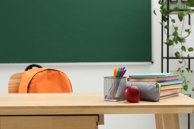 Photo of Different school stationery and red apple on wooden table near blackboard indoors