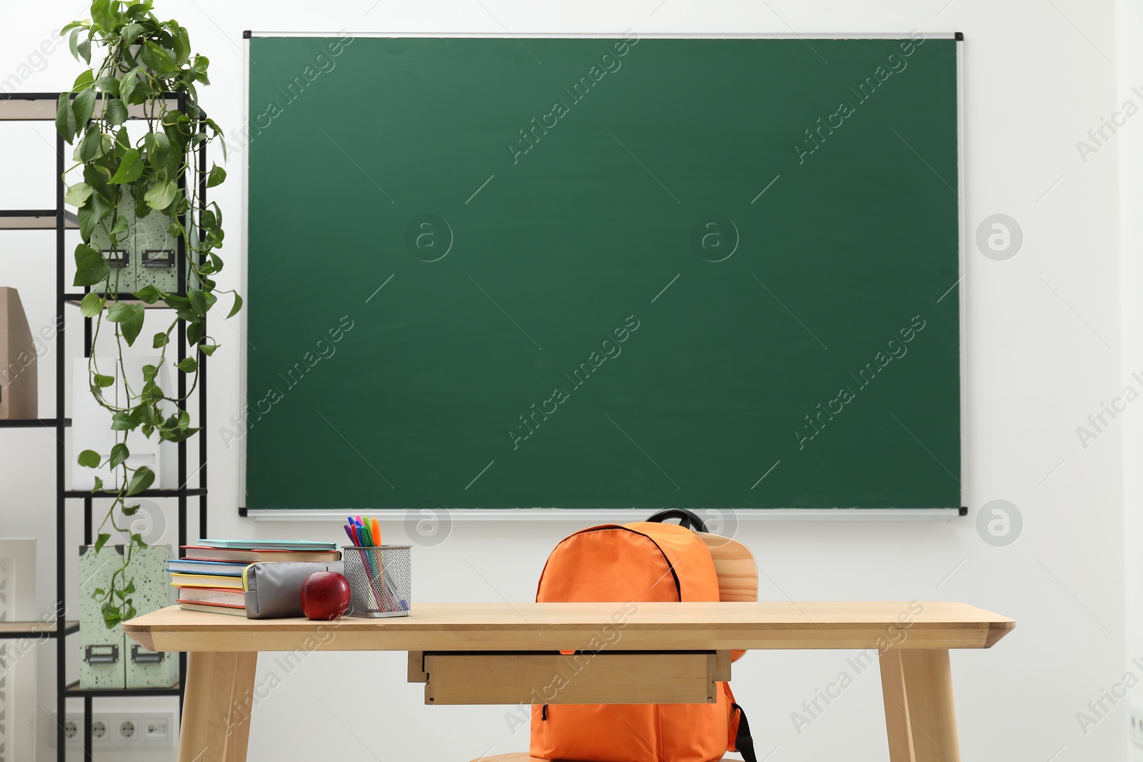 Different school stationery and red apple on wooden table near blackboard indoors Photo of Different school stationery and red apple on wooden table near blackboard indoors