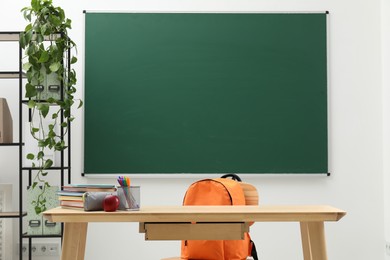 Photo of Different school stationery and red apple on wooden table near blackboard indoors