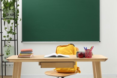 Photo of Different school stationery and red apple on wooden table near blackboard indoors
