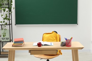 Photo of Different school stationery and red apple on wooden table near blackboard indoors