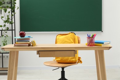 Photo of Different school stationery and red apple on wooden table near blackboard indoors