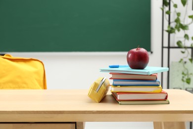 Photo of Different school stationery and red apple on wooden table near blackboard, space for text