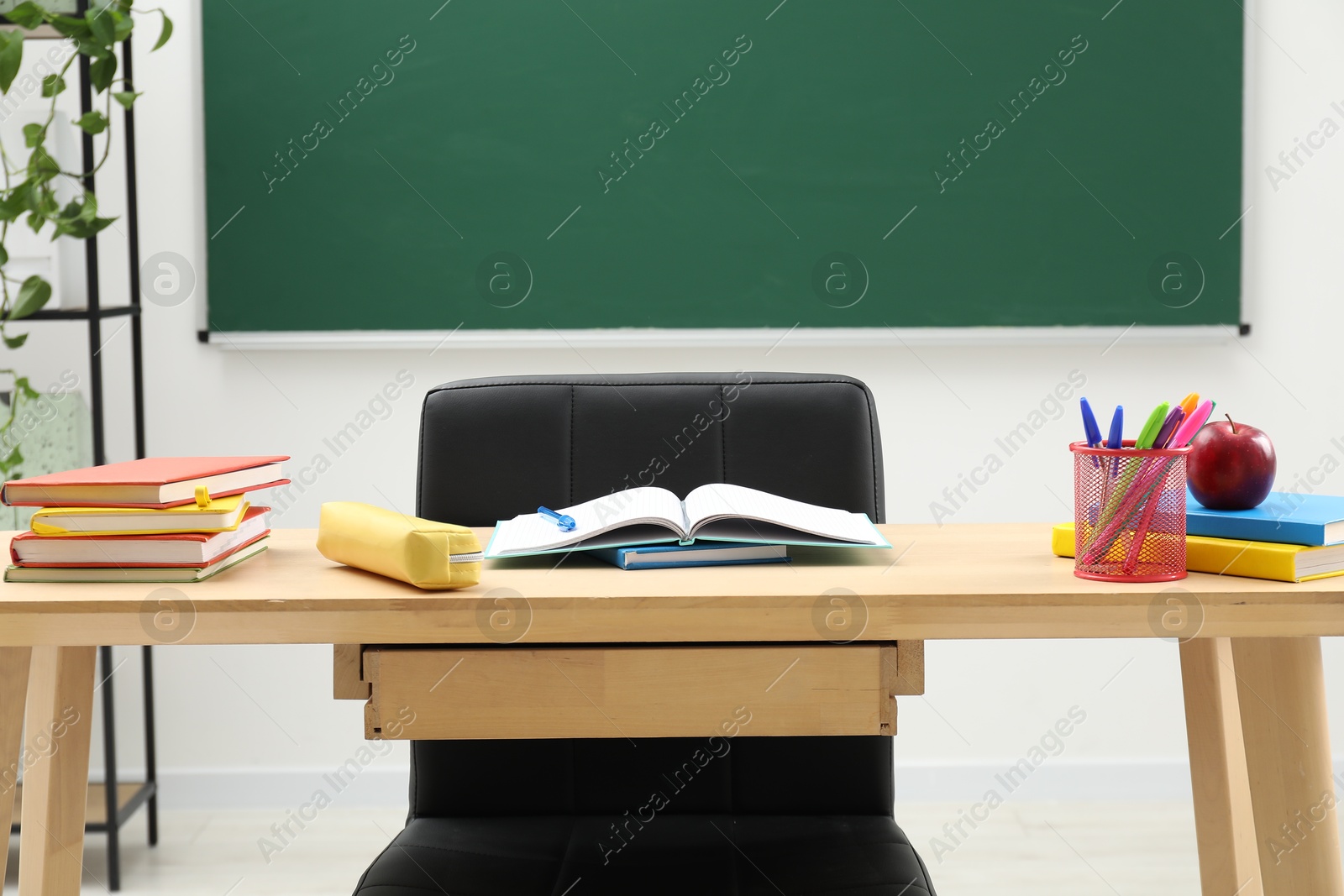 Different school stationery and red apple on wooden table near blackboard Photo of Different school stationery and red apple on wooden table near blackboard