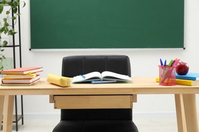 Photo of Different school stationery and red apple on wooden table near blackboard
