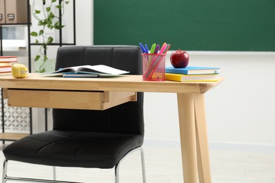 Photo of Different school stationery and red apple on wooden table near blackboard