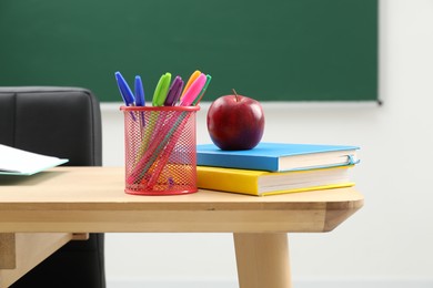 Photo of Different school stationery and red apple on wooden table near blackboard