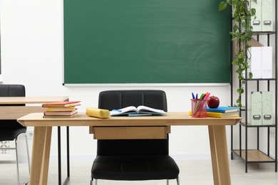 Photo of Different school stationery and red apple on wooden table near blackboard indoors
