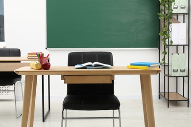 Photo of Different school stationery and red apple on wooden table near blackboard indoors
