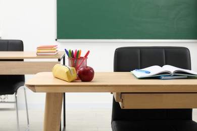 Photo of Different school stationery and red apple on wooden table near blackboard indoors