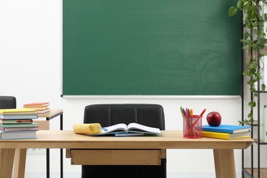 Photo of Different school stationery and red apple on wooden table near blackboard indoors