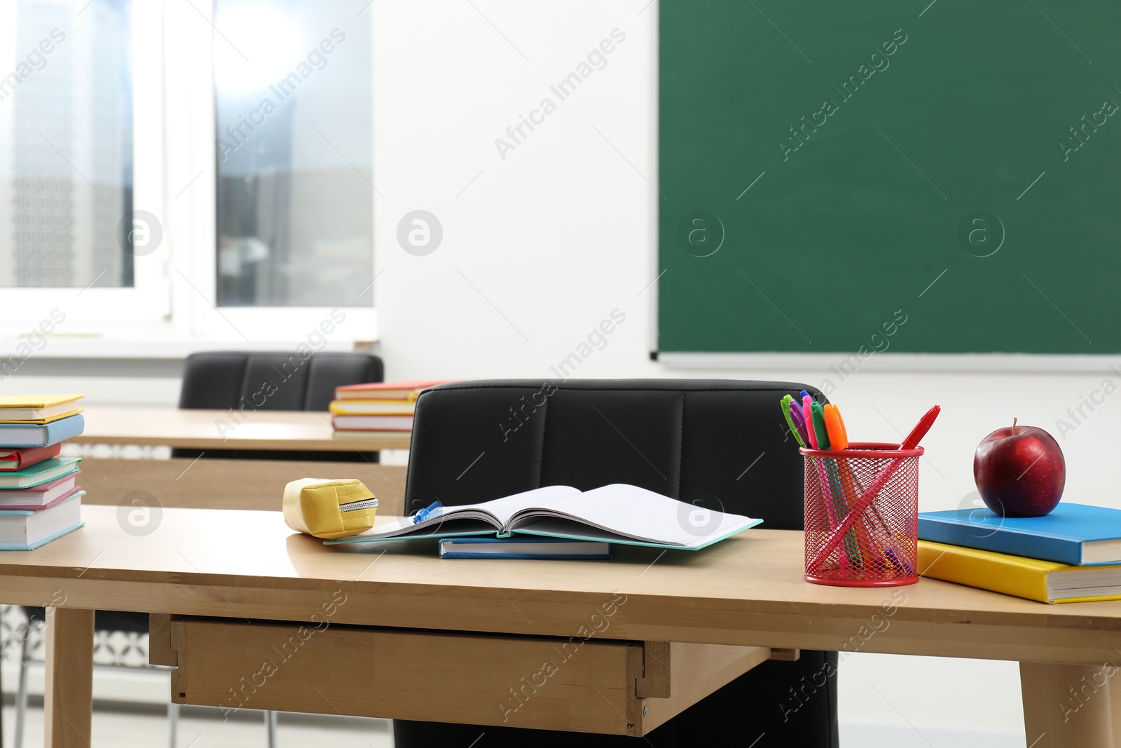 Different school stationery and red apple on wooden table near blackboard indoors Photo of Different school stationery and red apple on wooden table near blackboard indoors