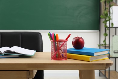 Photo of Different school stationery and red apple on wooden table near blackboard indoors