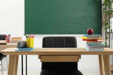 Photo of Different school stationery and red apple on wooden table near blackboard indoors