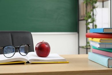 Photo of Different books, glasses and red apple on wooden table near blackboard indoors