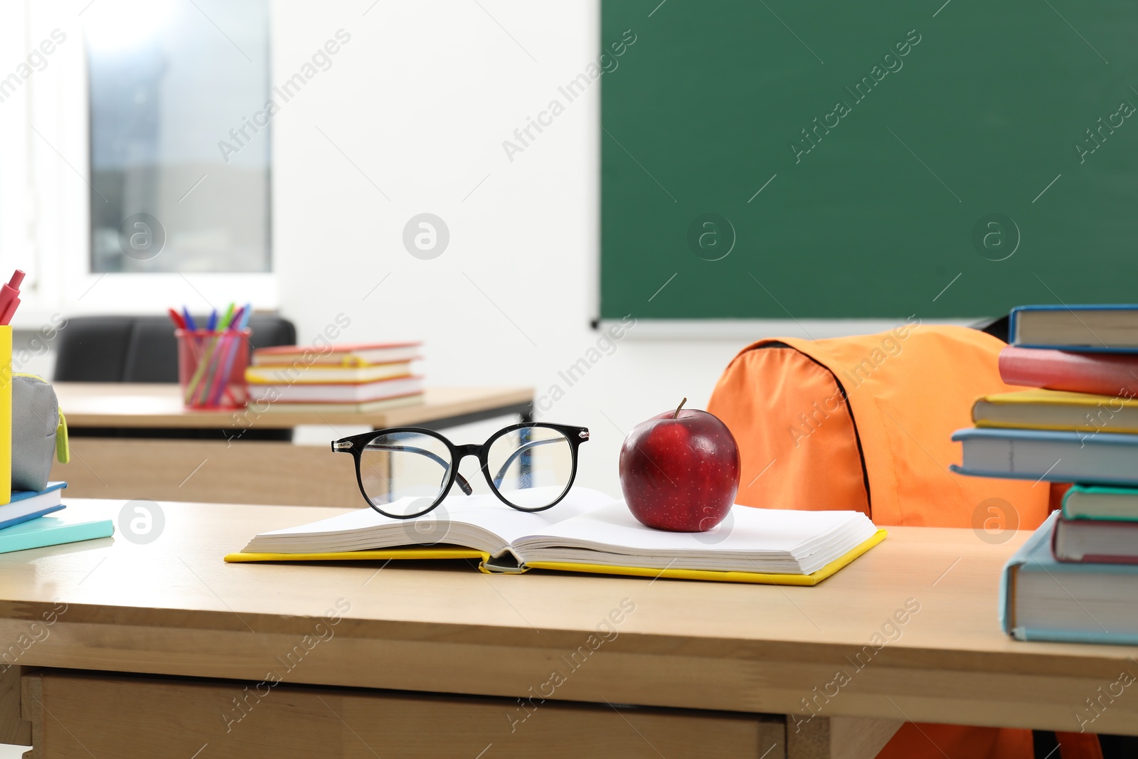 Different school stationery, glasses and red apple on wooden table near blackboard indoors Photo of Different school stationery, glasses and red apple on wooden table near blackboard indoors