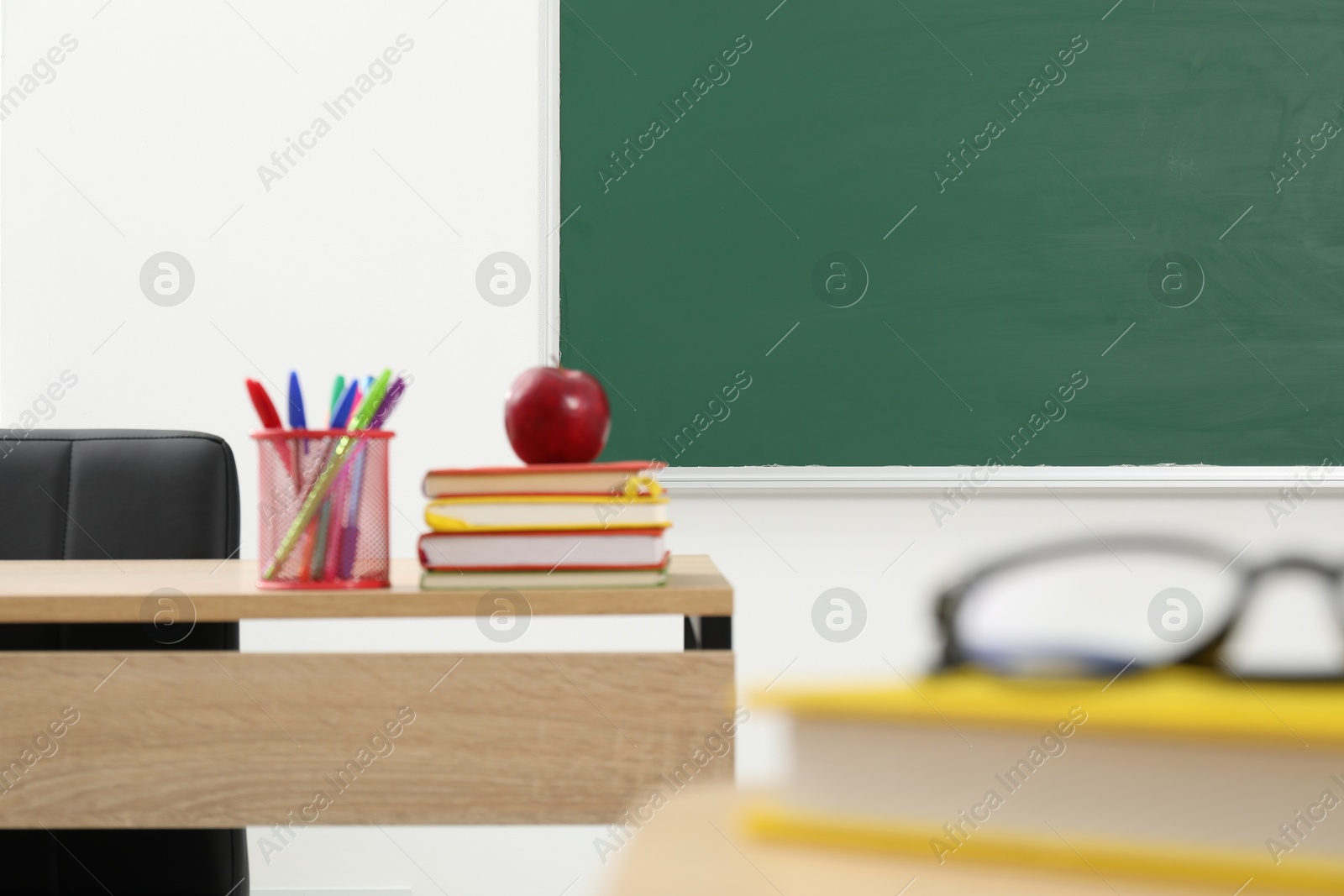 Different school stationery and red apple on wooden table near blackboard indoors Photo of Different school stationery and red apple on wooden table near blackboard indoors