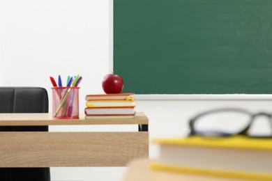 Photo of Different school stationery and red apple on wooden table near blackboard indoors