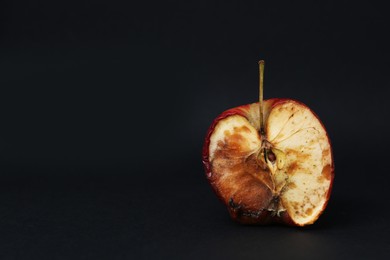 Photo of Half of spoiled apple on black background. Space for text