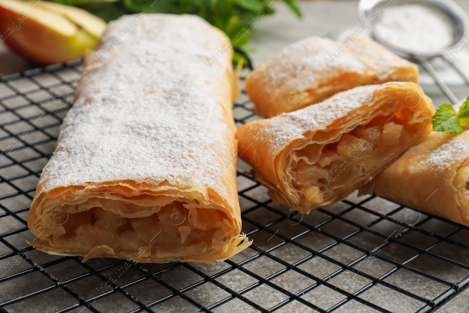 Tasty apple strudels with powdered sugar and mint on grey table, closeup Photo of Tasty apple strudels with powdered sugar and mint on grey table, closeup
