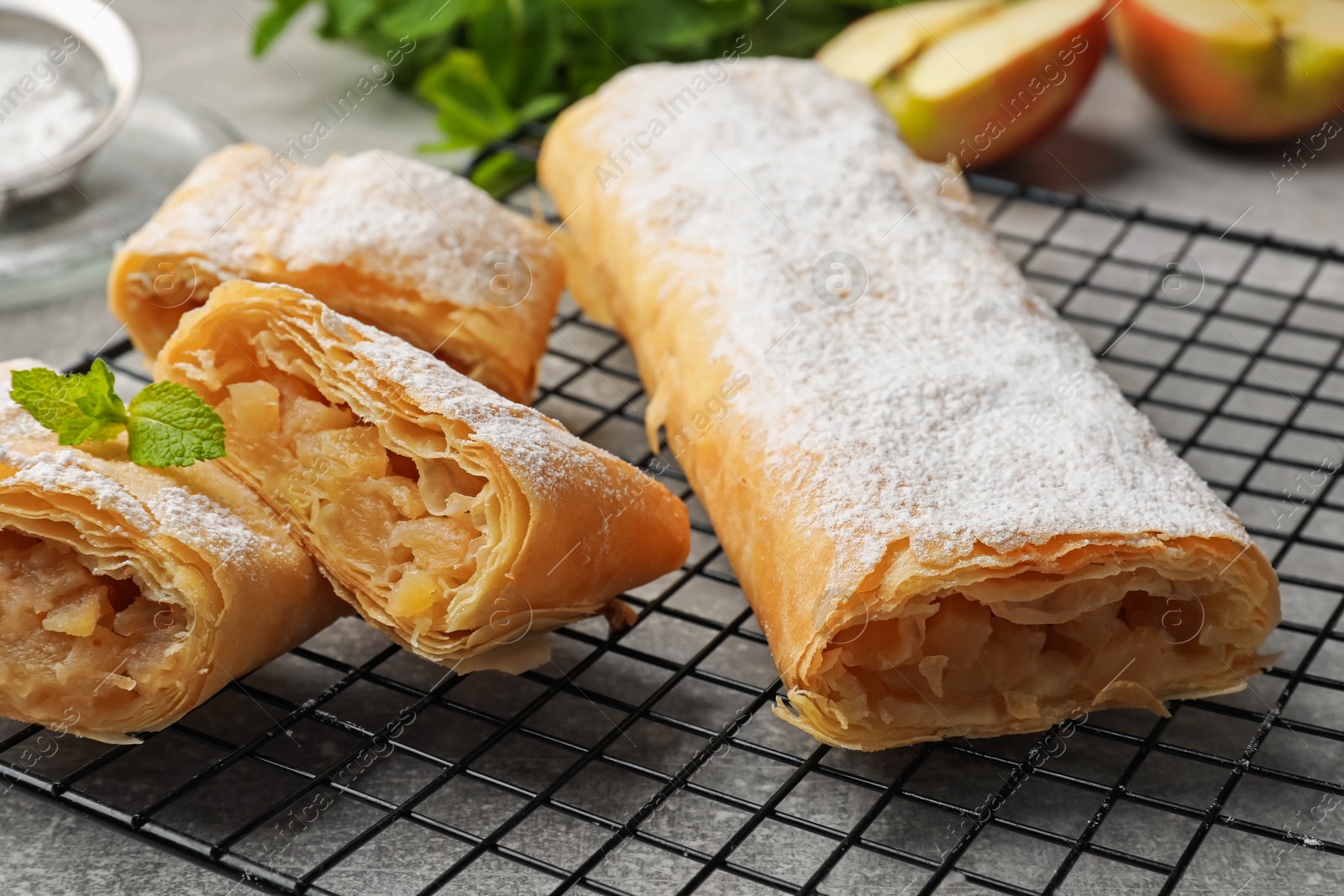 Tasty apple strudels with powdered sugar and mint on grey table, closeup Photo of Tasty apple strudels with powdered sugar and mint on grey table, closeup