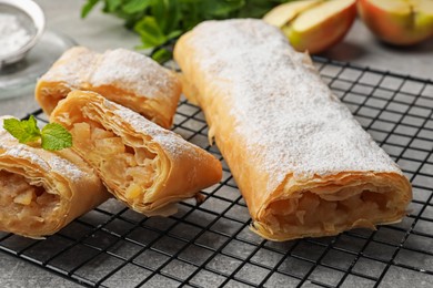 Photo of Tasty apple strudels with powdered sugar and mint on grey table, closeup