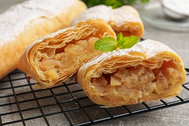 Photo of Tasty apple strudels with powdered sugar and mint on grey table, closeup